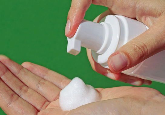Une main actionne un flacon-pompe blanc pour déposer de la mousse dans une paume ouverte.
