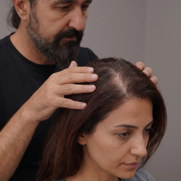A man parts a seated woman’s hair to examine her scalp.