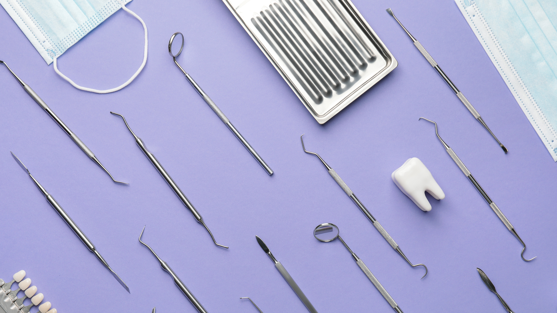 Dental instruments laid out on a tray against a purple background, seen from above
