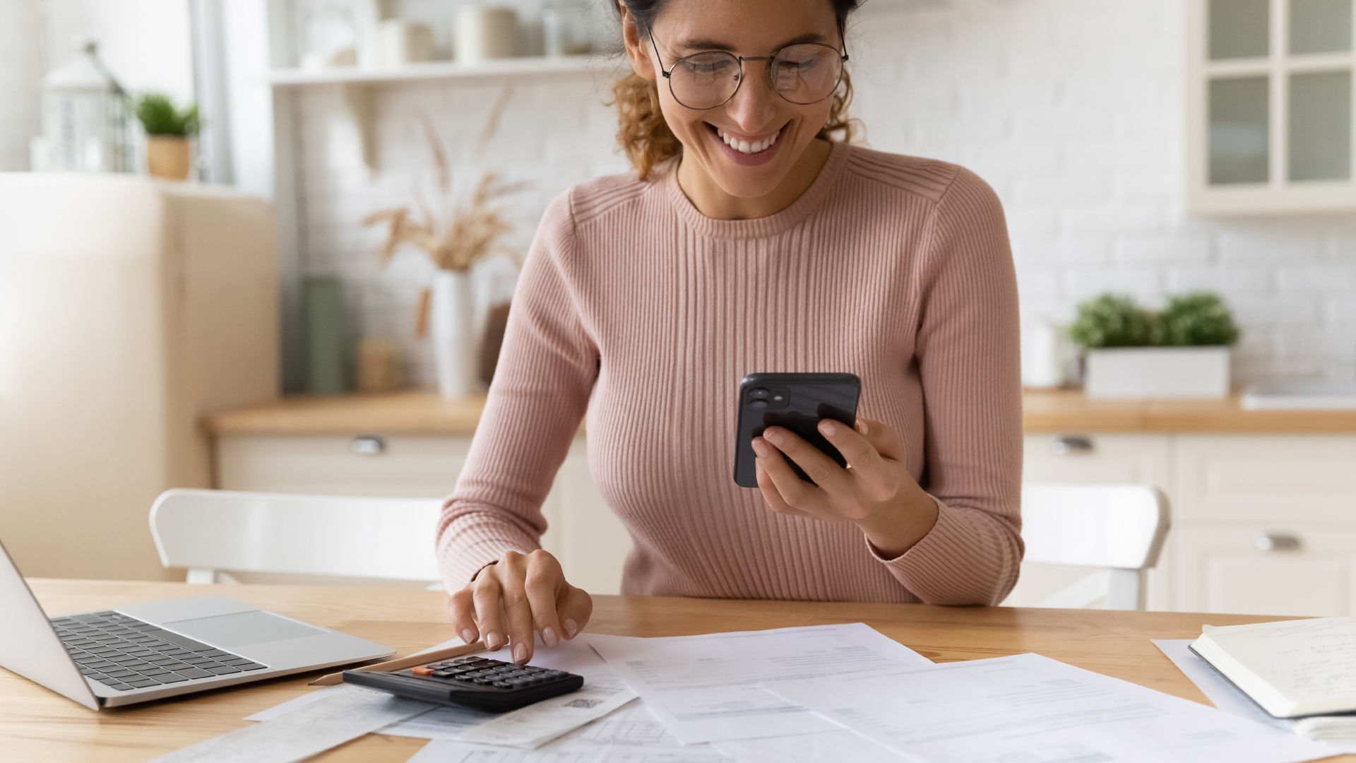 Une femme installée à son bureau avec un téléphone, une calculatrice et des documents, en train de faire ses comptes