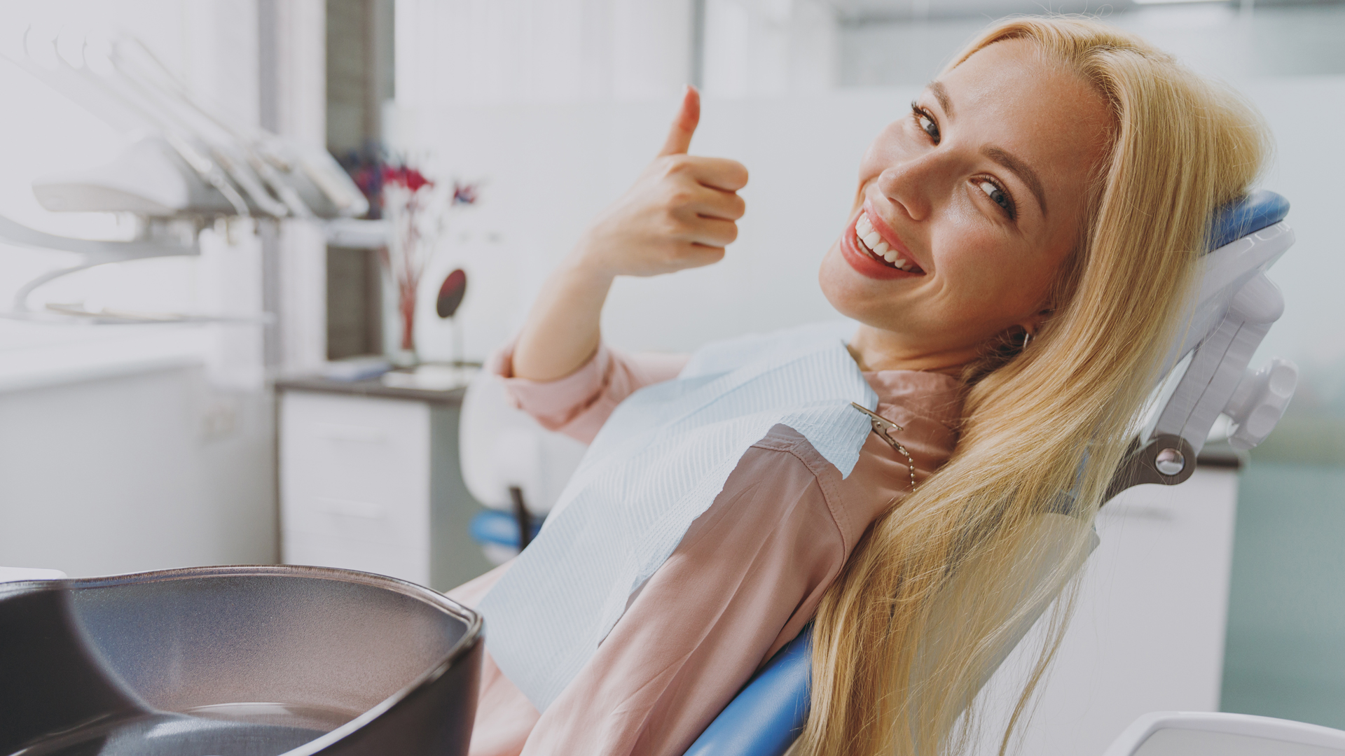 Blonde patient lying in a dental chair giving a thumbs-up to the camera