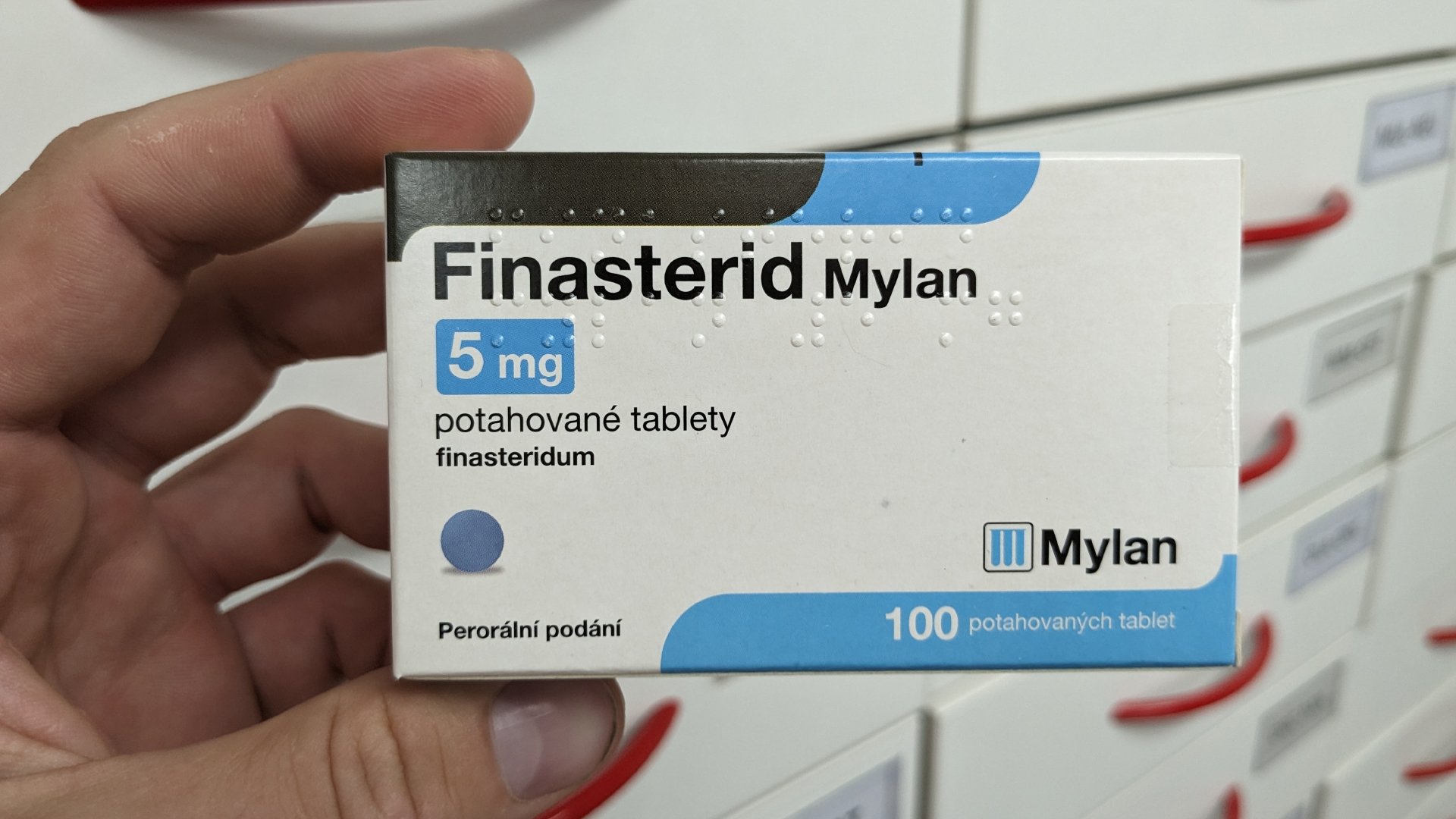 Main tenant une boîte portant la mention Finasterid Mylan 5 mg