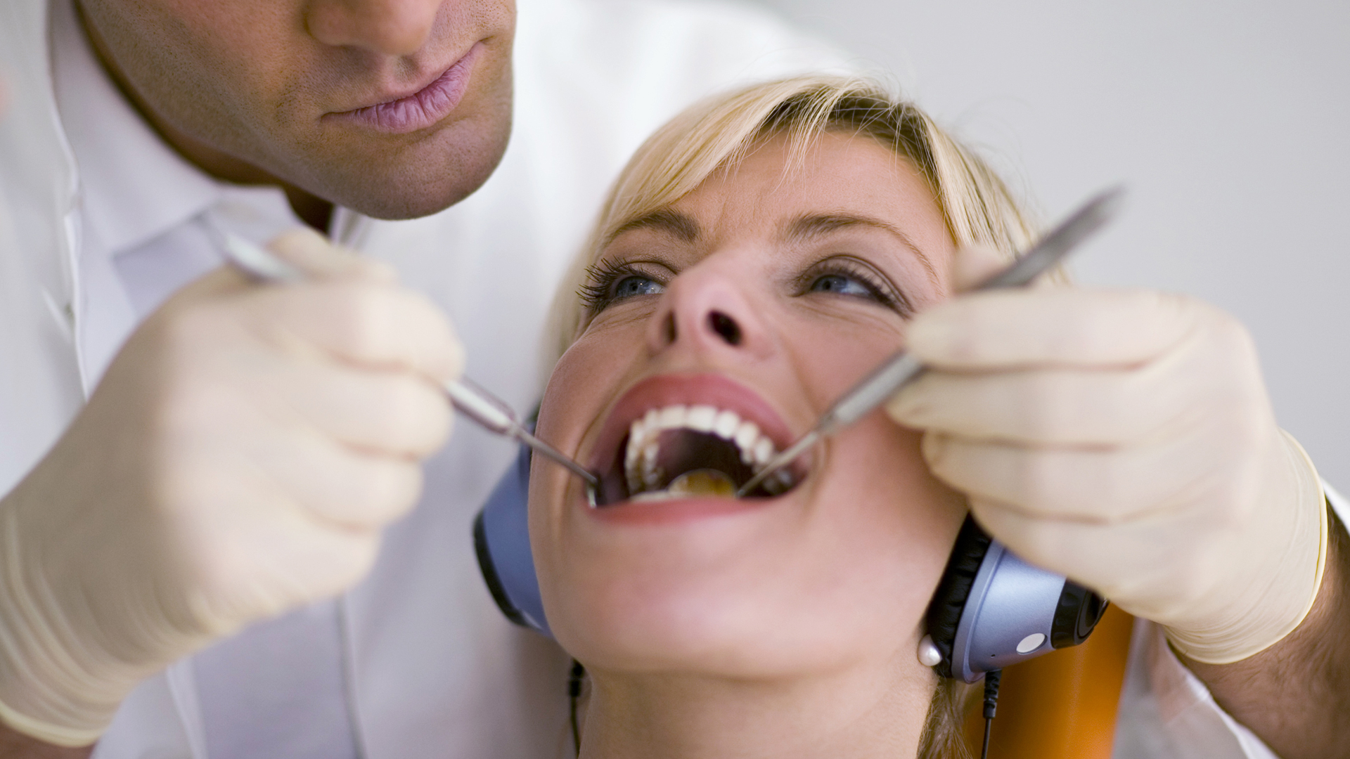 Dentist examining a reclined patient's mouth with a mirror and a probe