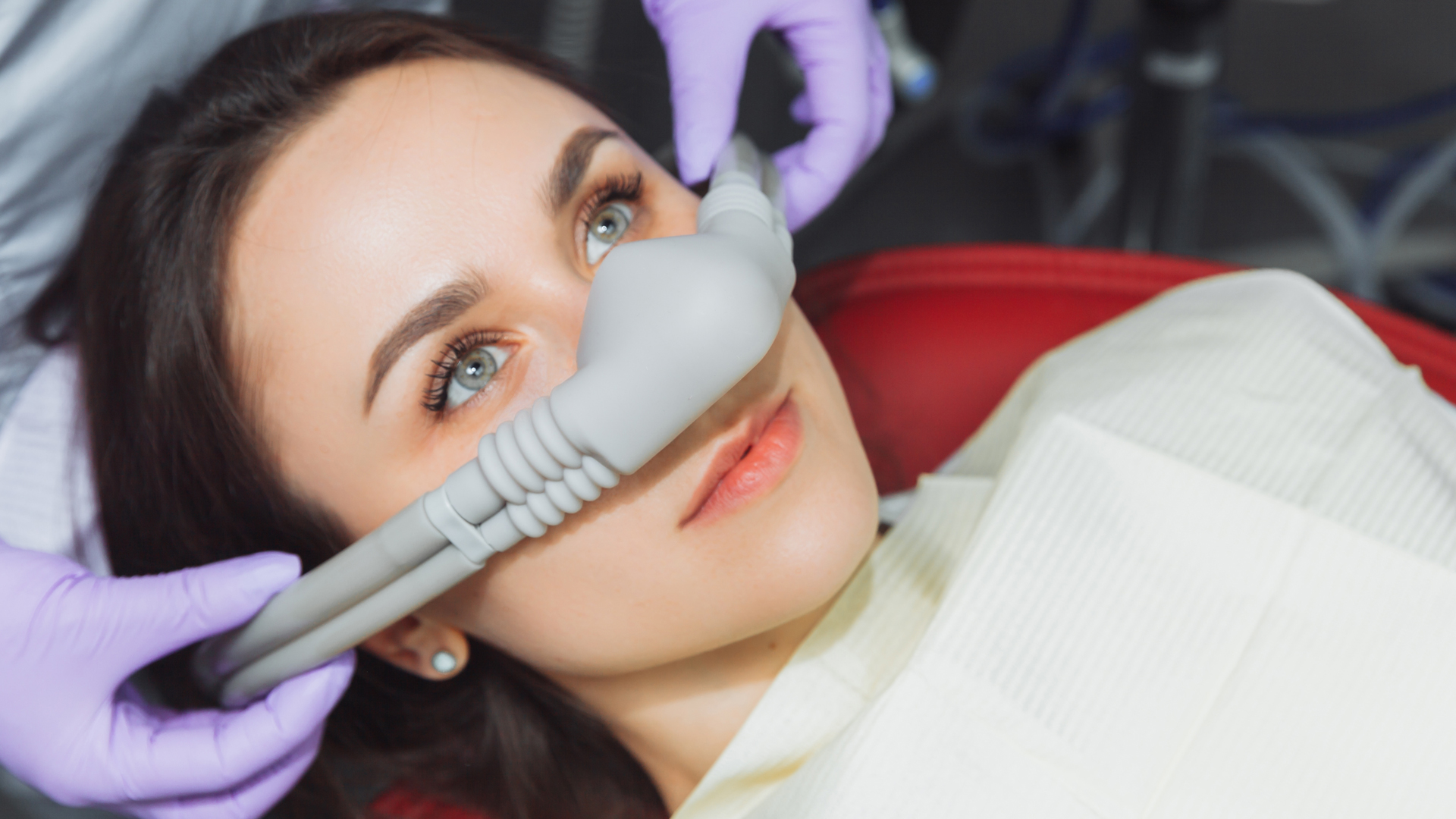 Patient reclined while a gloved hand places a nasal hood for inhalation sedation