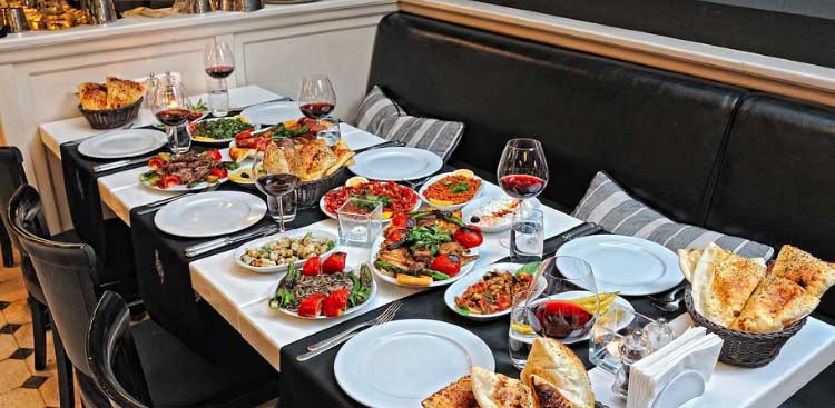 Banquettes and laid tables in a restaurant, spread with meze, grilled meats, baskets of bread and glasses of red wine