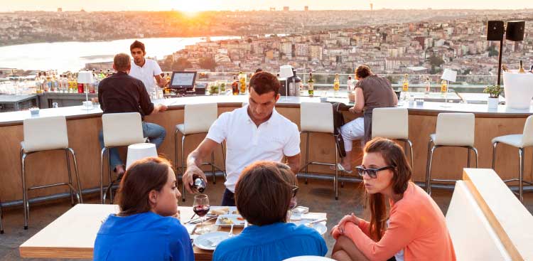 Terrasse de restaurant sur un toit d’Istanbul au coucher du soleil, tables occupées face au panorama de la ville