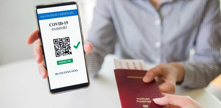 Main tenant un smartphone affichant un certificat de vaccination « Covid-19 passport » avec QR code, et une autre main tenant un passeport bordeaux