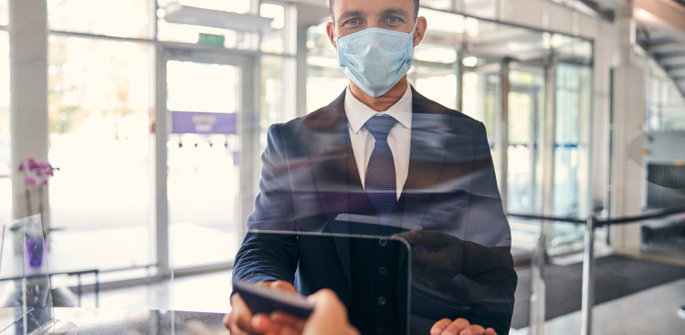 Panneau de verre d’un terminal d’aéroport, un homme en costume portant un masque chirurgical consulte son téléphone