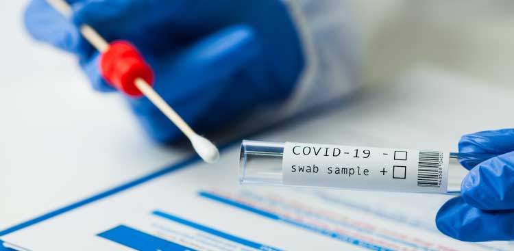 Blue-gloved hands holding a swab and a tube labelled ‘COVID-19 swab sample’ above a form