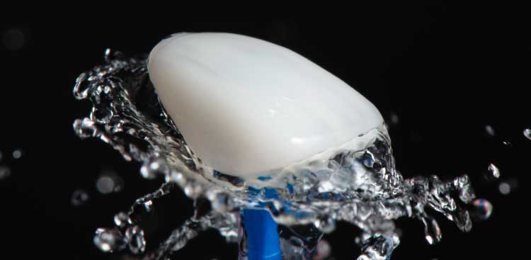 Coque de céramique dentaire blanche traversée par une gerbe d’eau, sur fond noir