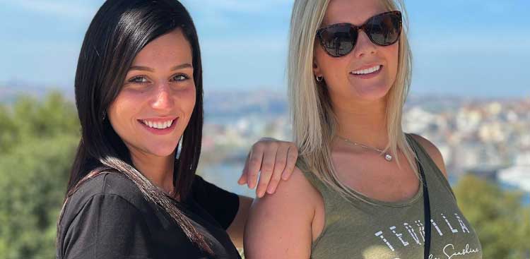 Océanie and Marie posing side by side, smiling, in front of a panorama of the city by the water