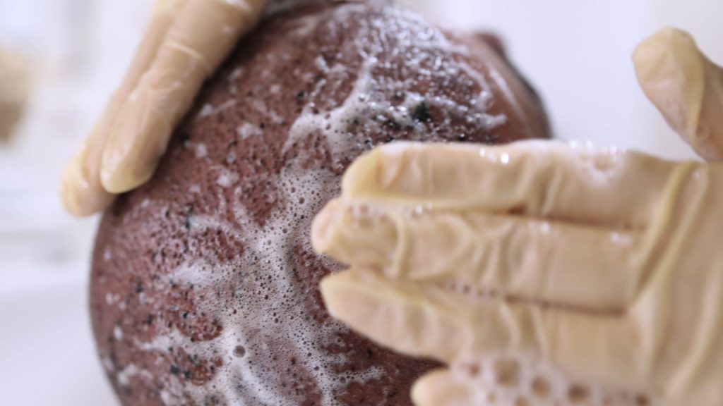 Mains gantées répartissant une mousse sur un cuir chevelu