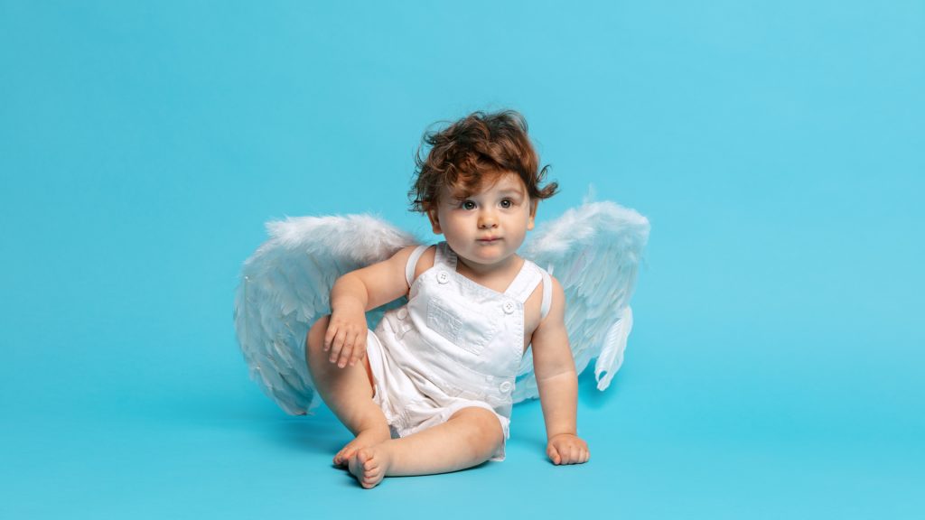 Un jeune enfant portant de petites ailes d'ange blanches, assis sur fond bleu
