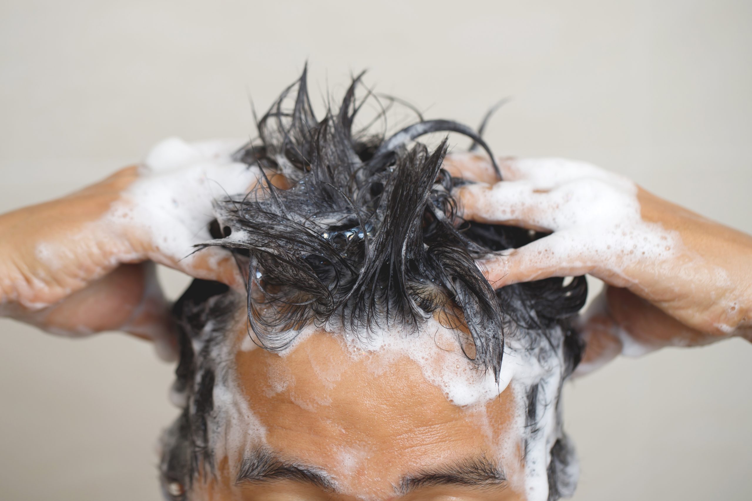 Gros plan sur deux mains frottant des cheveux mouillés couverts de mousse.