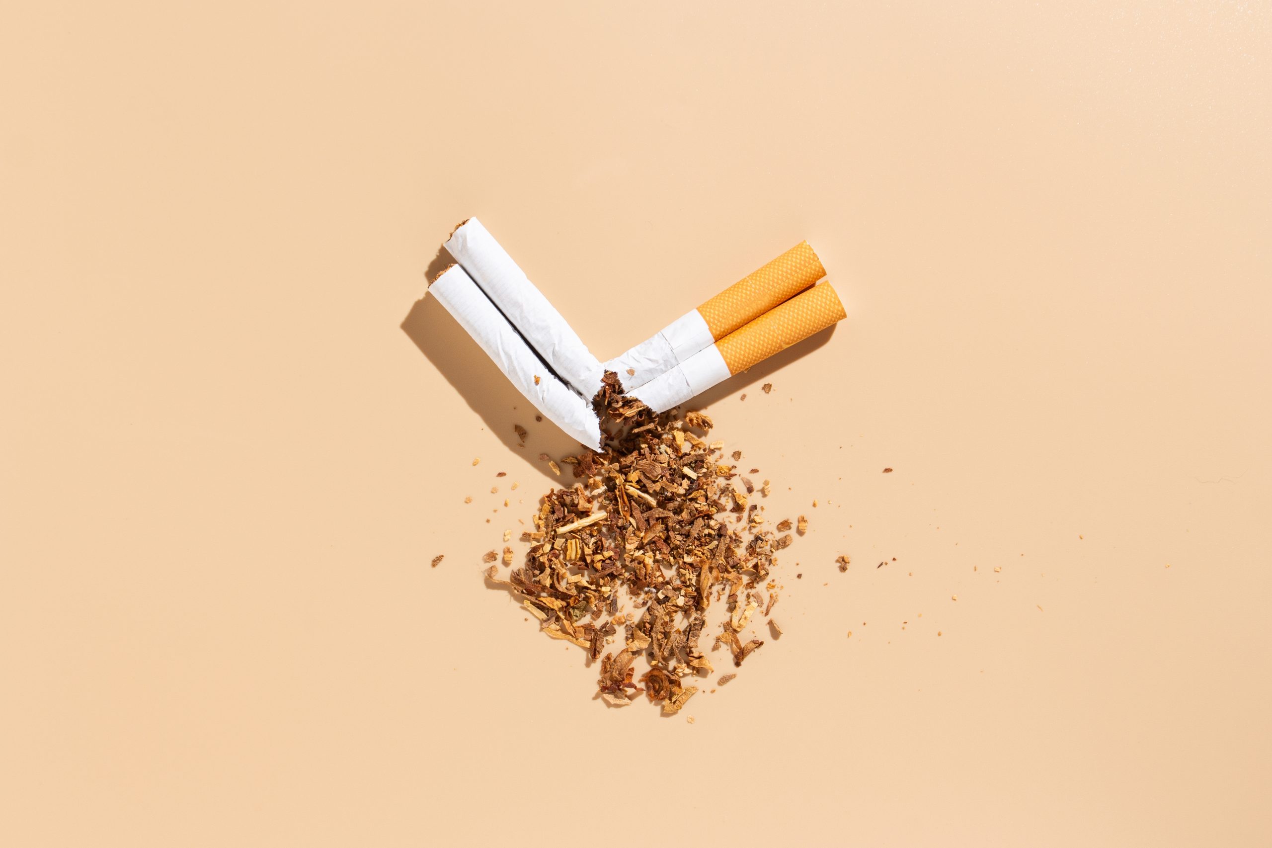 Deux cigarettes brisées et du tabac éparpillé sur un fond beige.