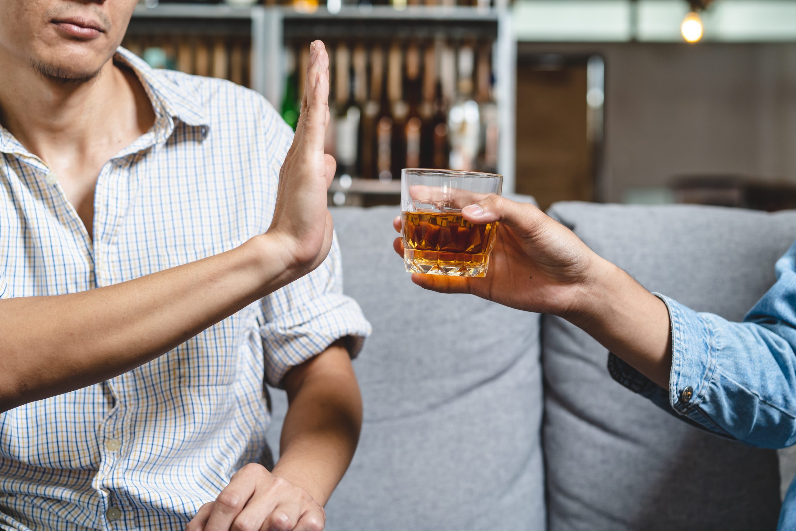 A seated person raises an open palm to decline a glass of amber drink offered by another person.