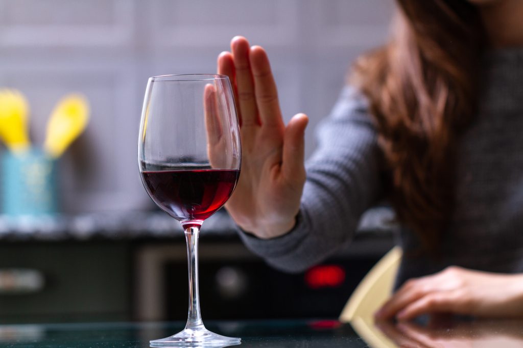 A person raises an open palm in front of a glass of red wine in a gesture of refusal.