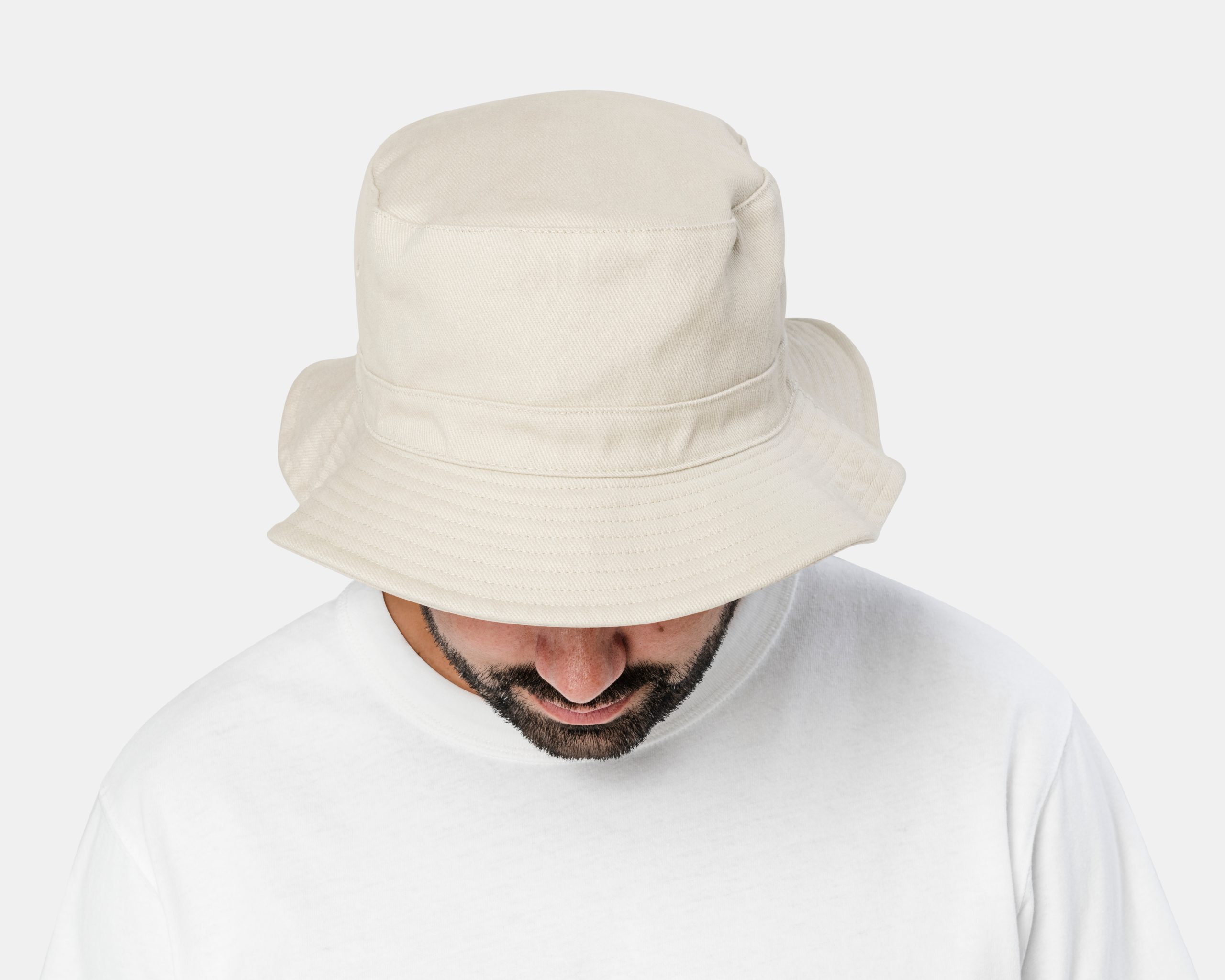 Homme tête penchée vers le bas, portant un grand bob beige à calotte haute et un tee-shirt blanc.
