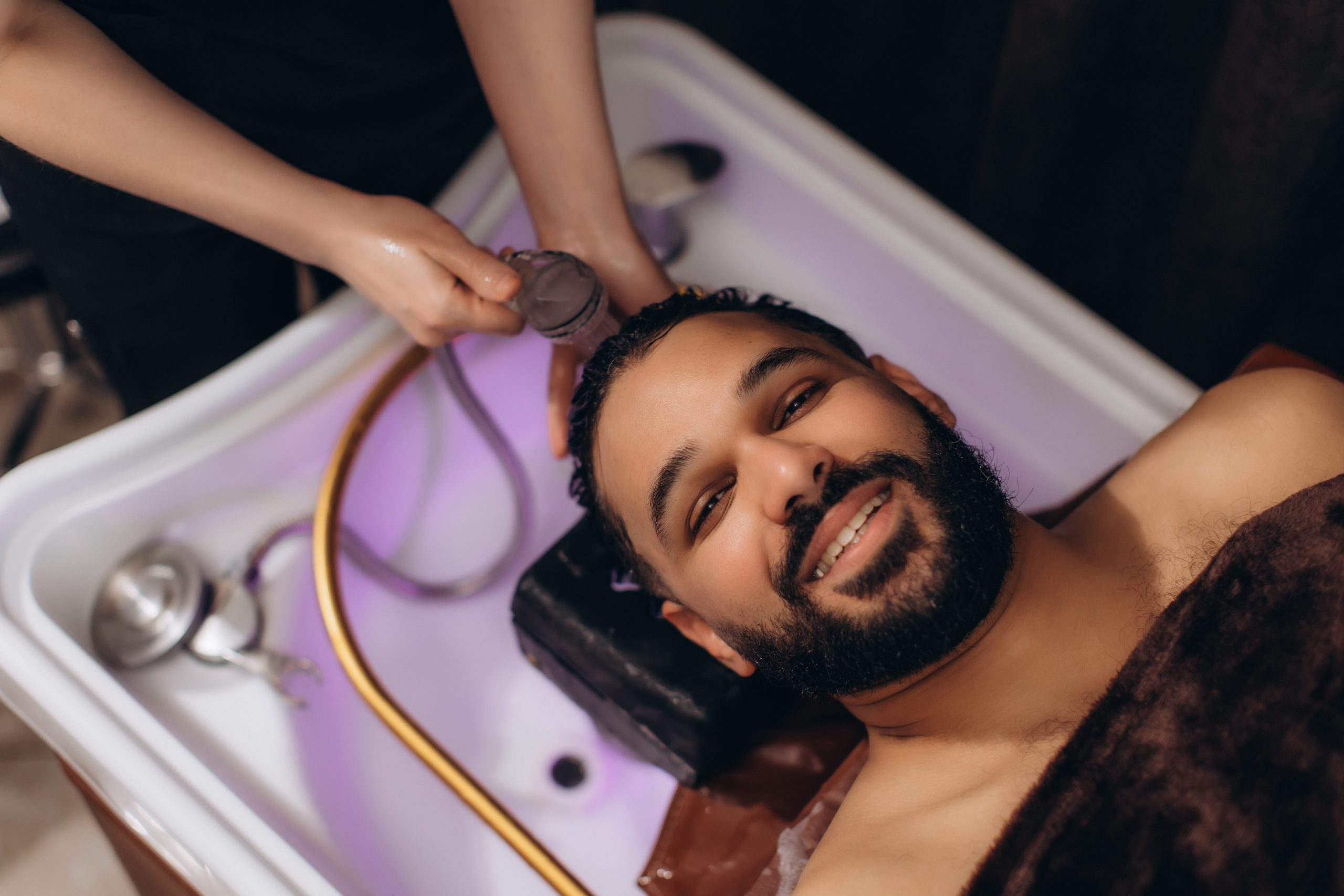 Un homme allongé au bac à shampooing se fait rincer les cheveux avec une douchette.