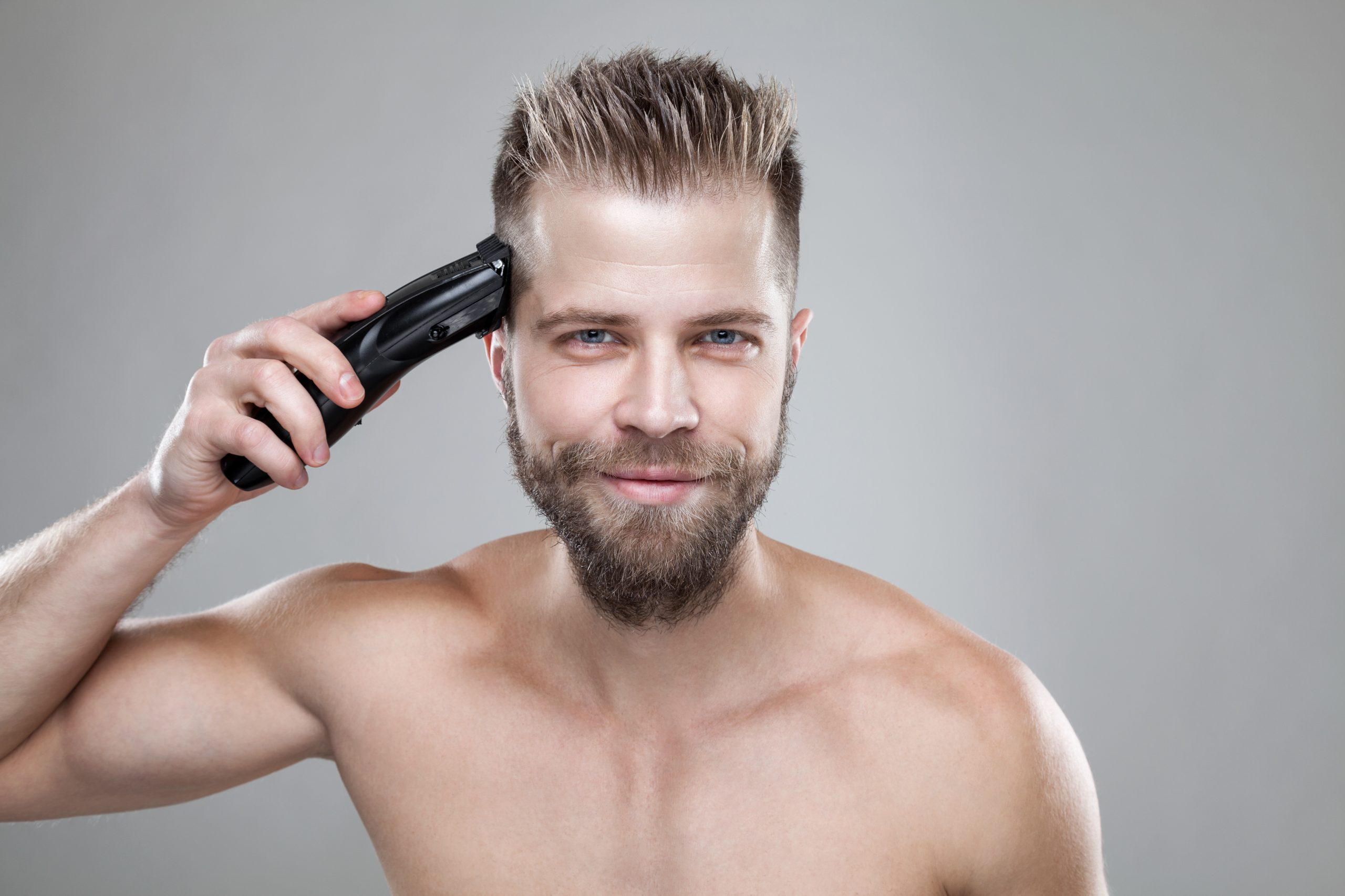 Homme barbu passant une tondeuse électrique sur le côté de sa tête, près de la tempe.