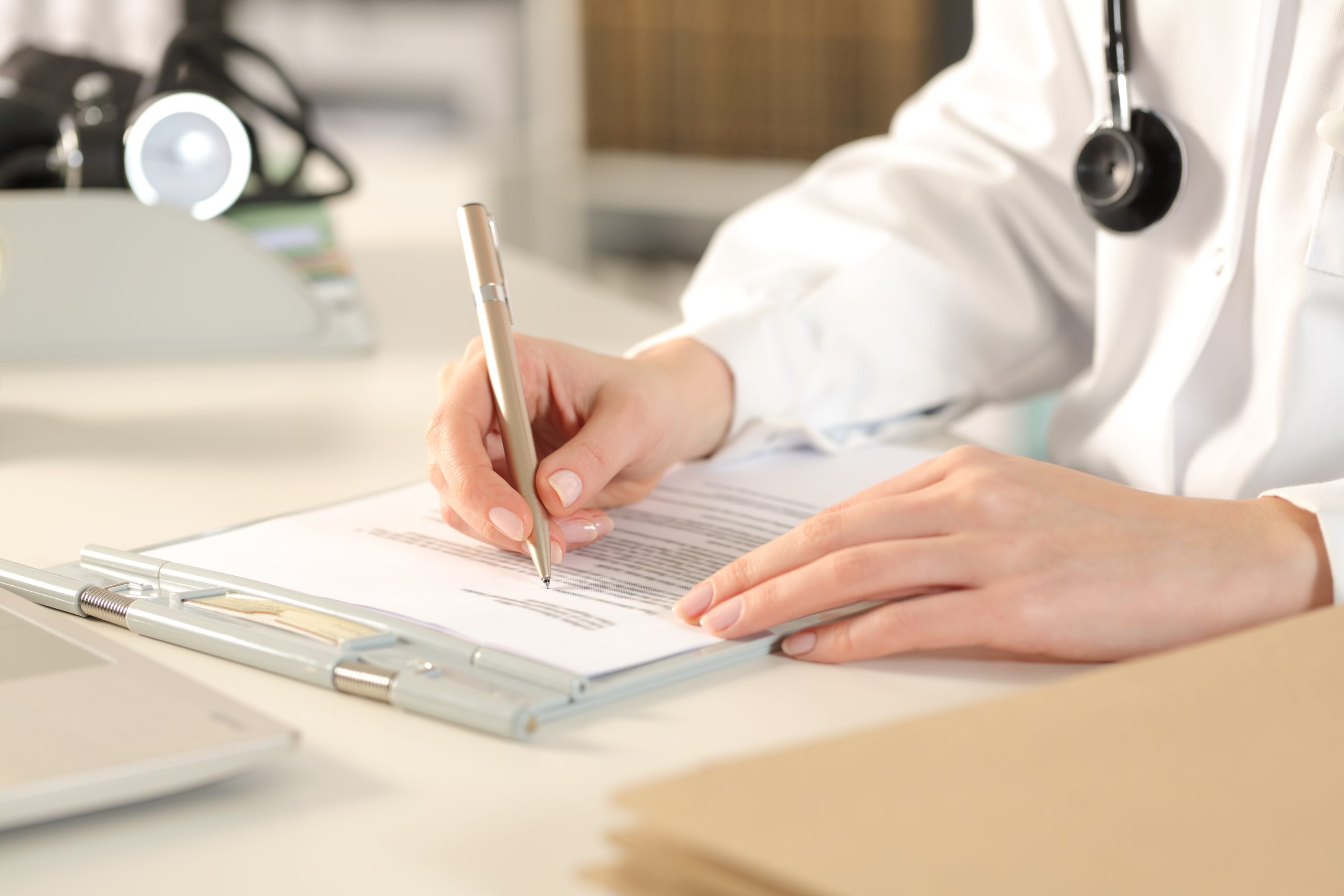 Une personne en blouse blanche avec un stéthoscope remplit un formulaire sur un porte-bloc.