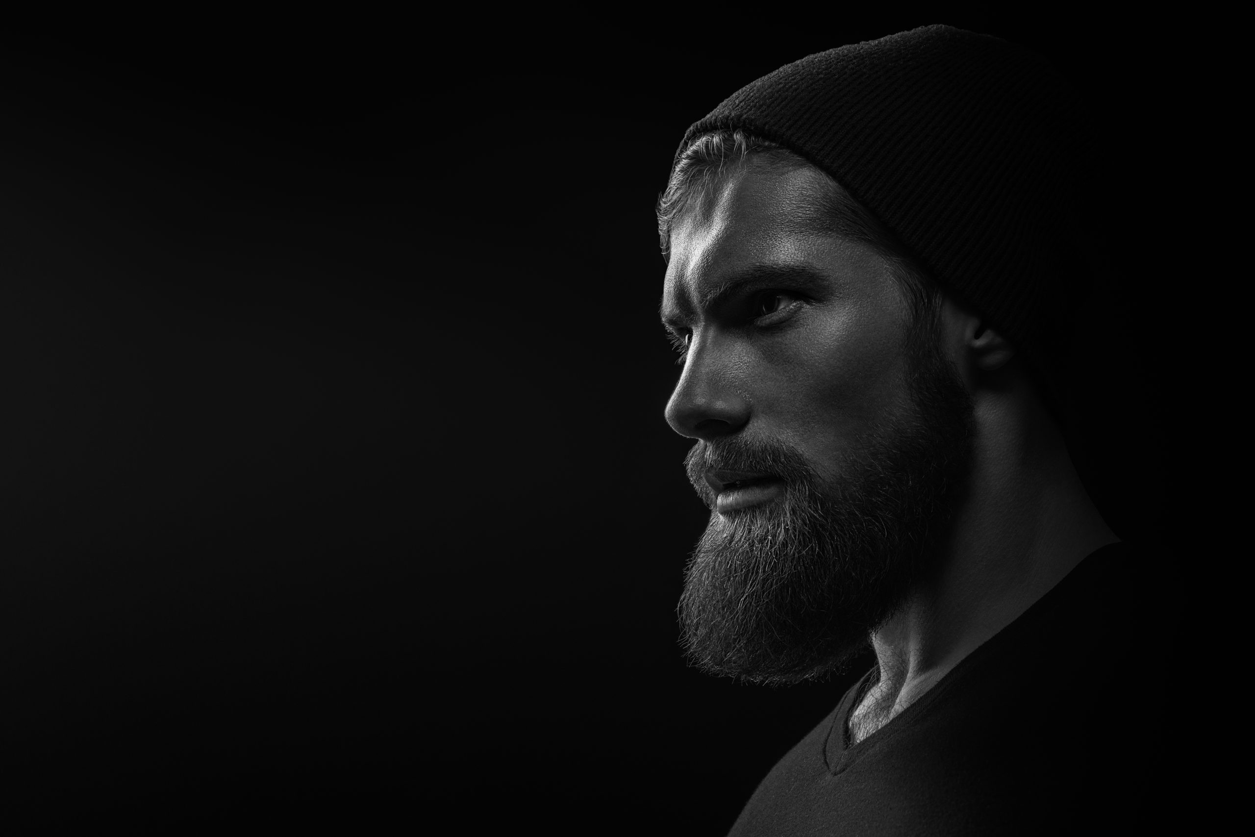 Portrait en noir et blanc d’un homme barbu portant un bonnet sombre, vu de trois quarts.
