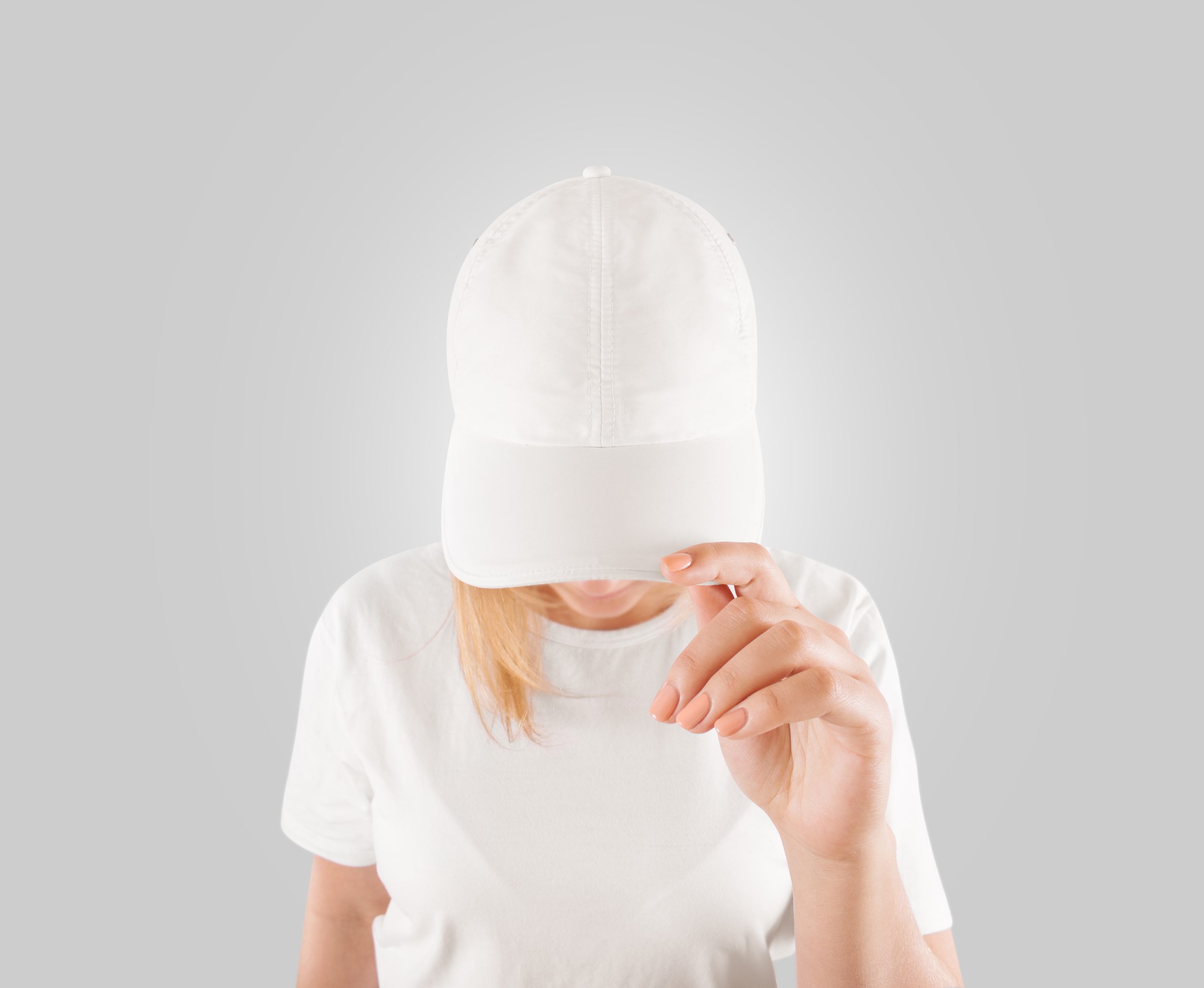 Personne tête baissée tenant entre les doigts la visière de sa casquette blanche, sur fond gris.